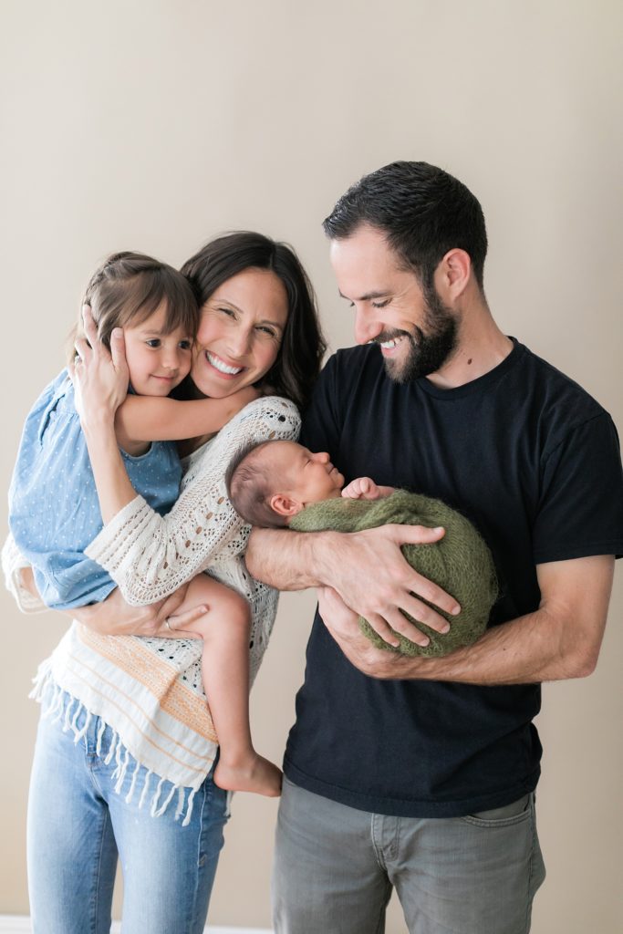 Happy family holding their two year old daughter and their smiling newborn. Newborn photography by Tayler Enerle Photography in Los Osos, California. Megan and Mason