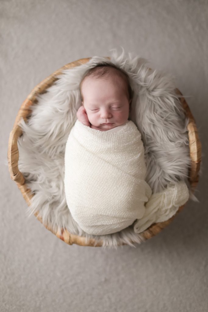 Newborn portrait of a baby wrapped in and posed in a basket. Photo taken by Tayler Enerle Photography in San Luis Obispo, California