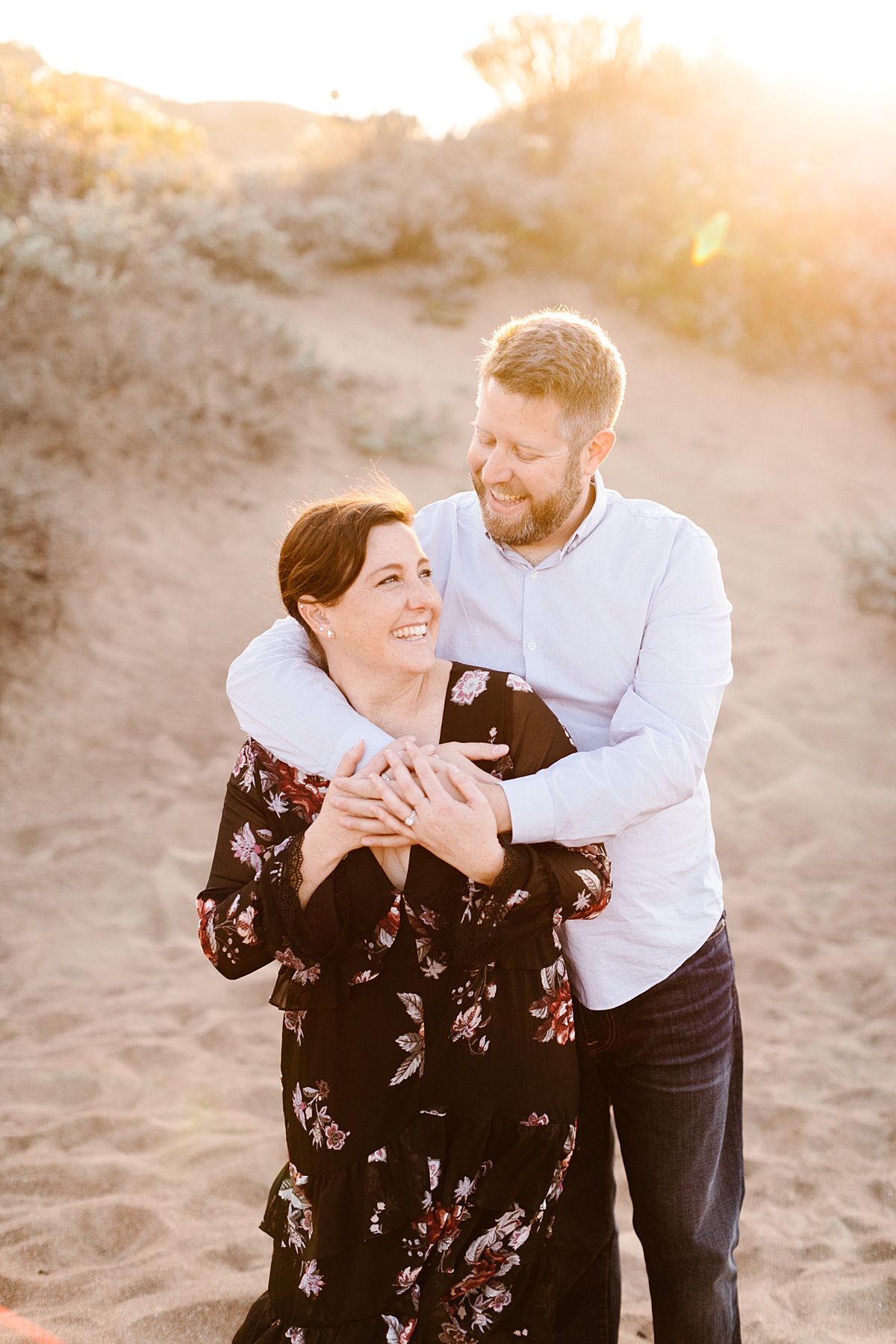 Happy couple embracing and smiling together during engagement session on the sand dunes in Los Osos, California