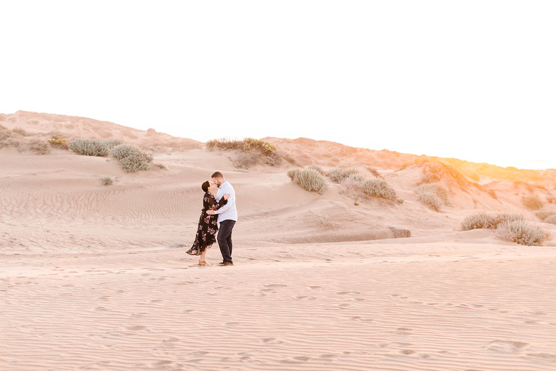 engaged couple embrace on los osos sand dunes at sunset