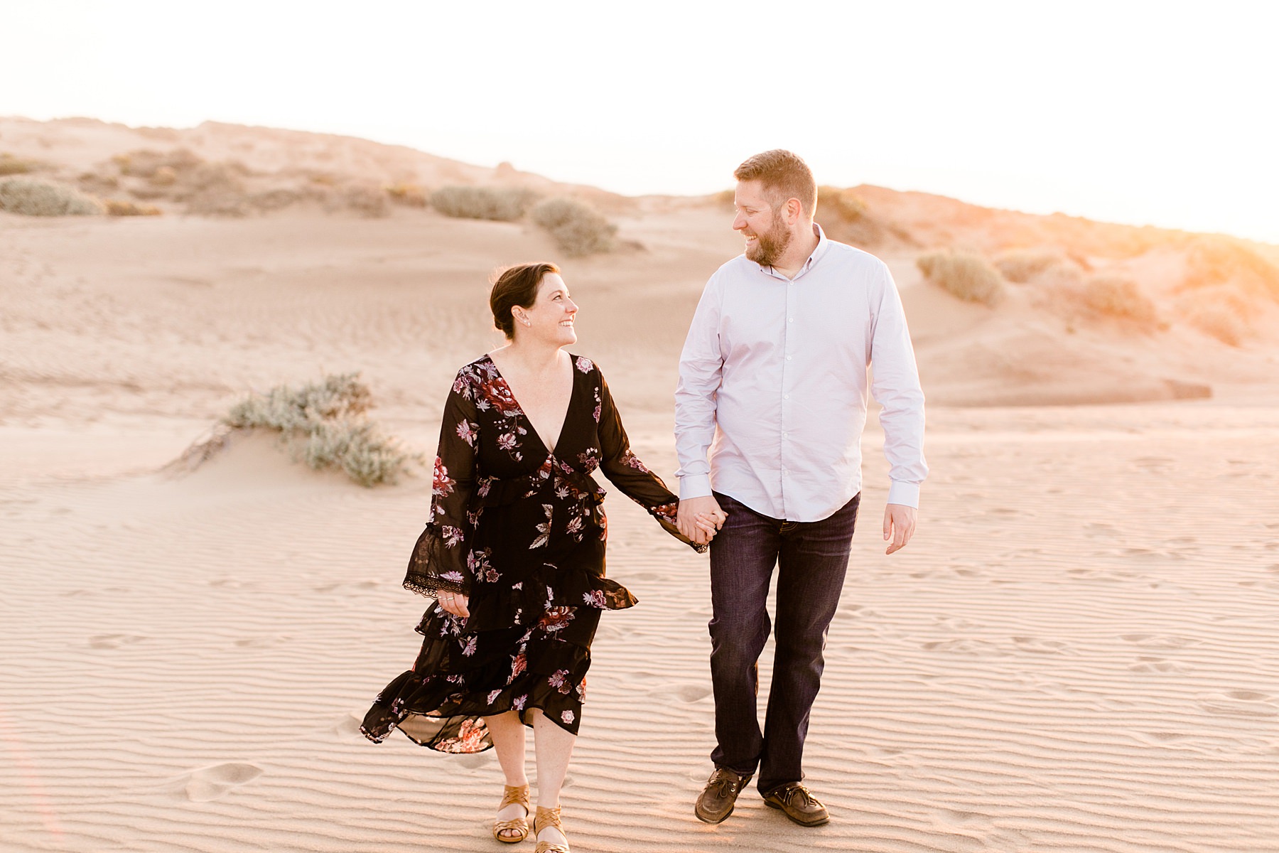 engaged couple walking hand in hand on the sand dunes in Los Osos, California at sunset