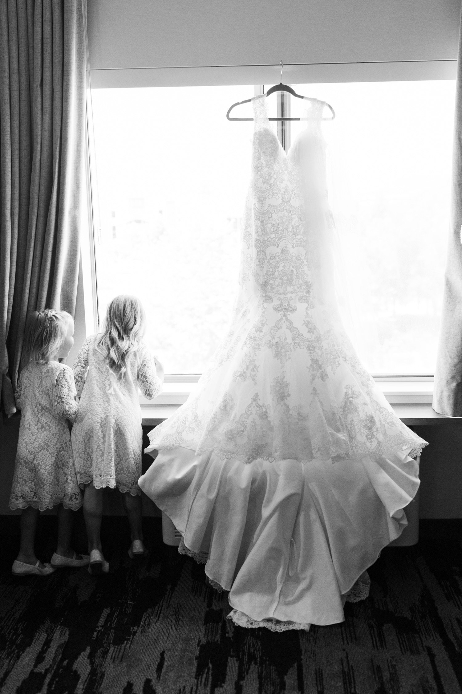 Flower girls looking out the window in expectation next to the bride's wedding dress