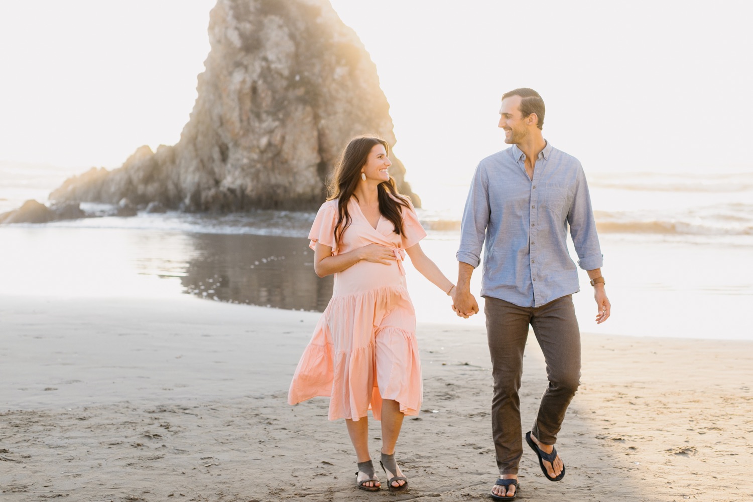 couple walking and smiling on the beach in Pismo, california at their maternity session with tayler enerle