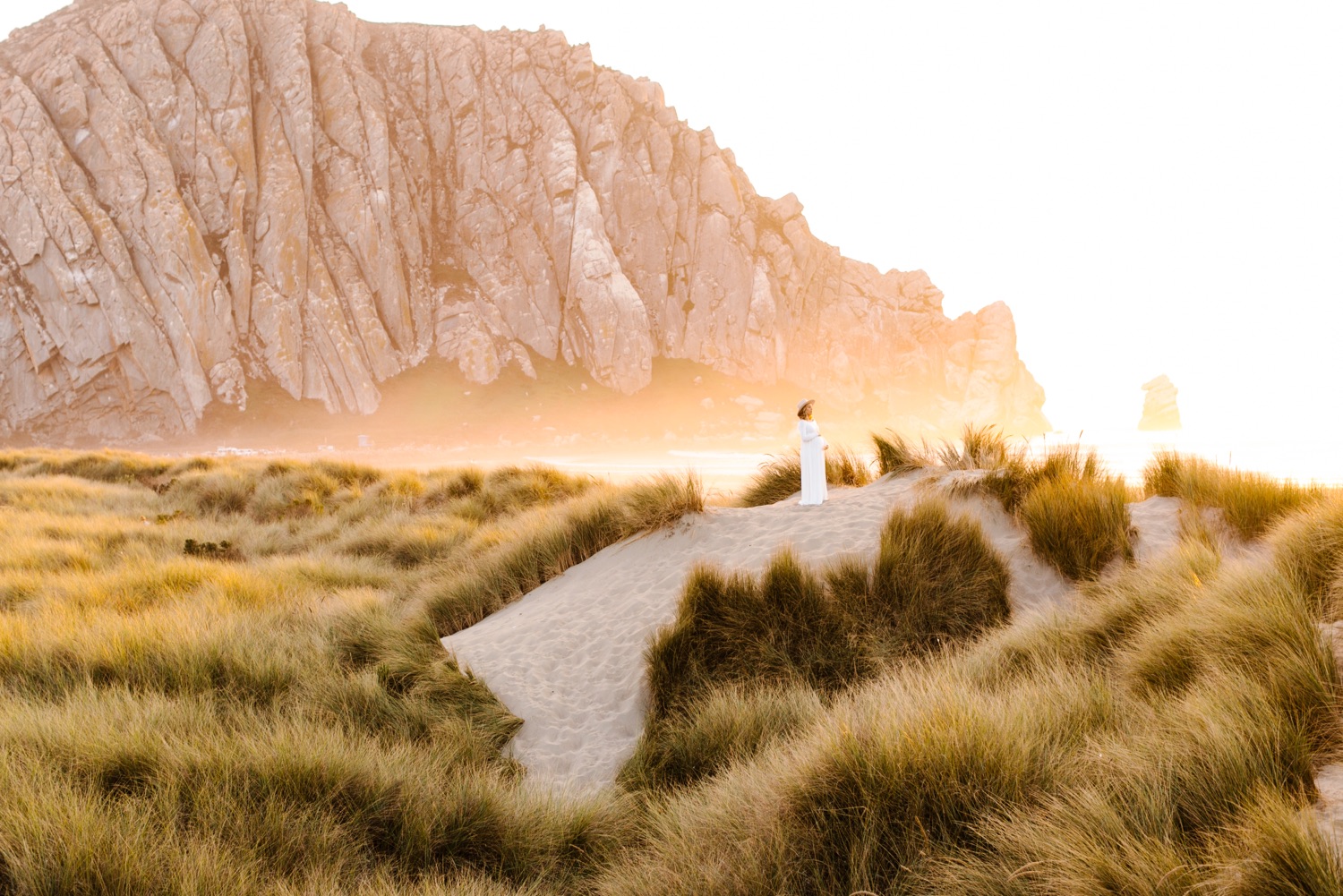 Wide panoramic image of expecting mother in the sand dunes in front of Morro Rock at Maternity session with Tayler Enerle