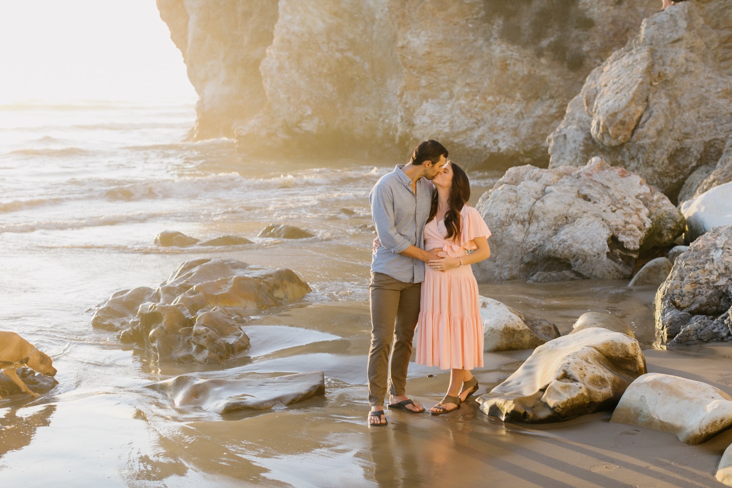 pismo beach maternity session where couple are embracing and kissing in front of the ocean and rocks