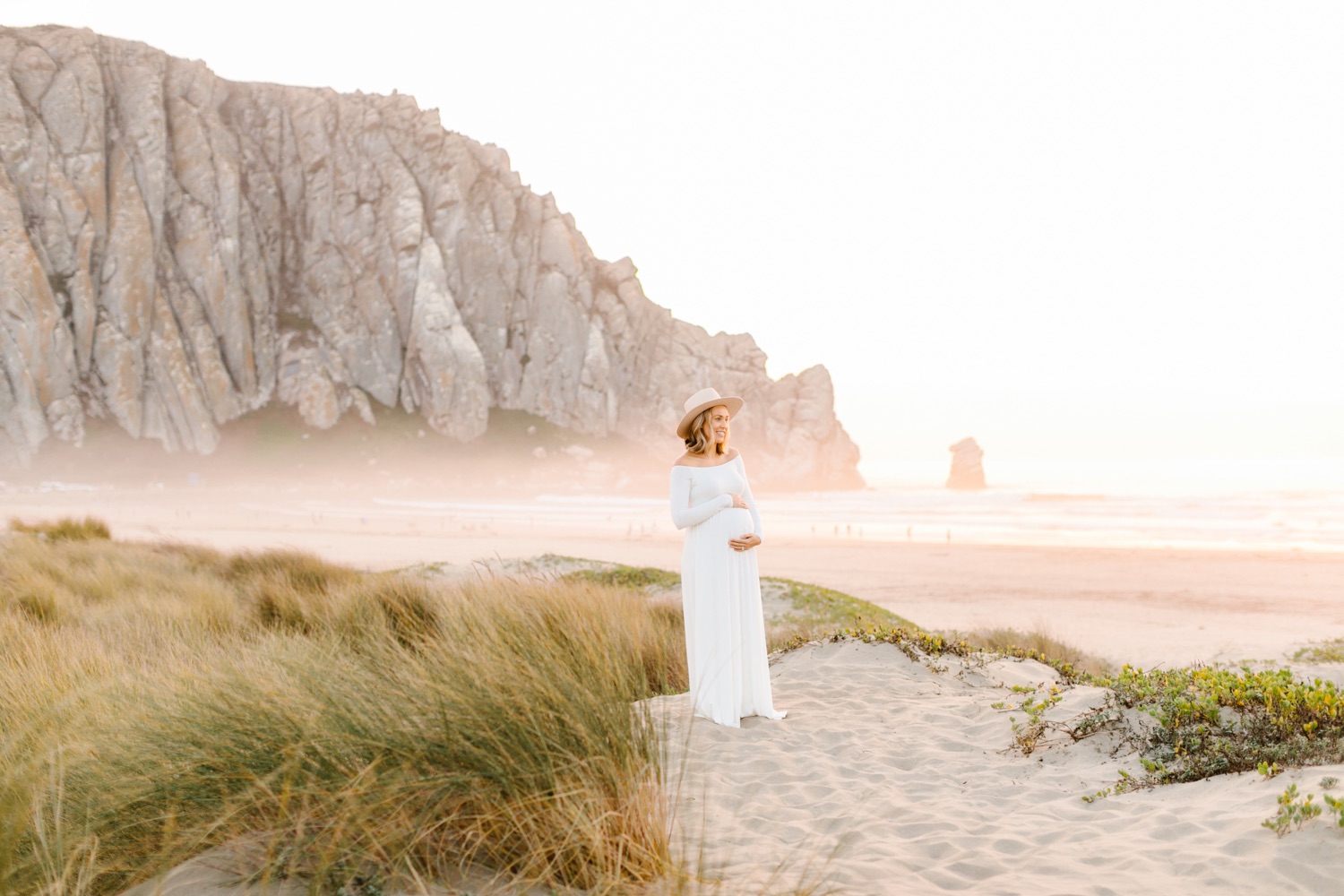 Expecting mother posing in front of morro rock at her maternity session with Tayler Enerle