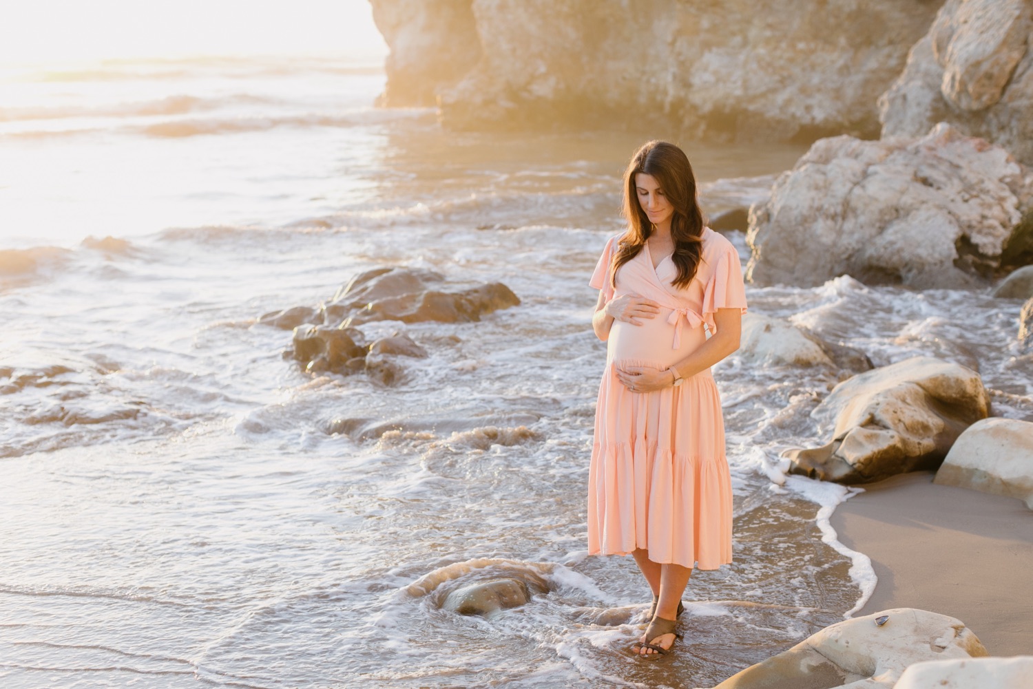 Pregnant woman embracing and looking at her belly at pismo beach