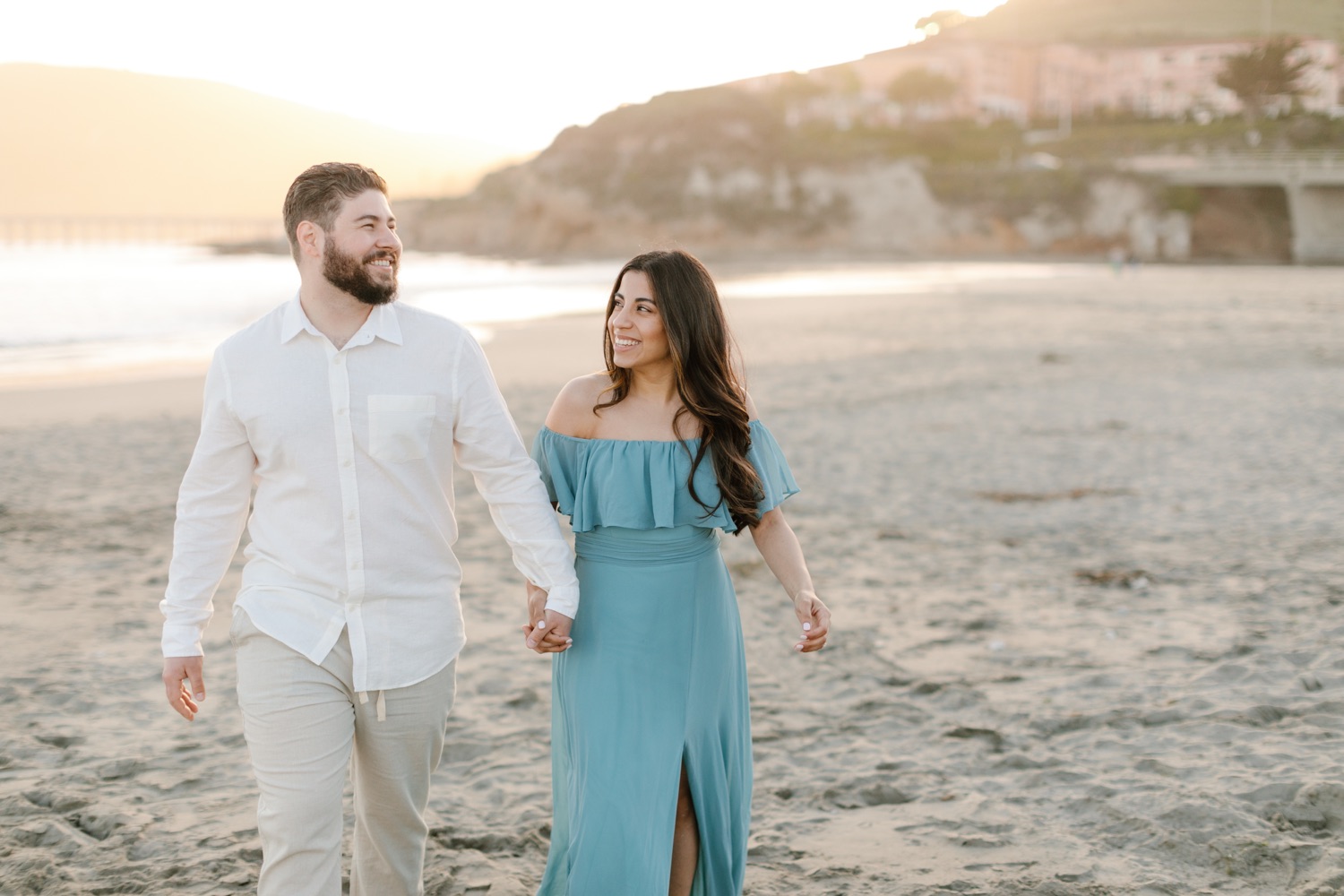 couple laughing hand in hand on the beach in Avila for their engagement session