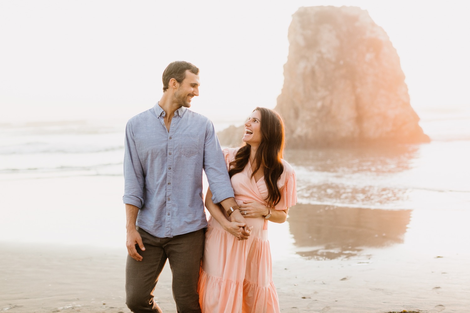 couple holding hands and laughing while walking at their maternity session at pismo beach, california by tayler enerle