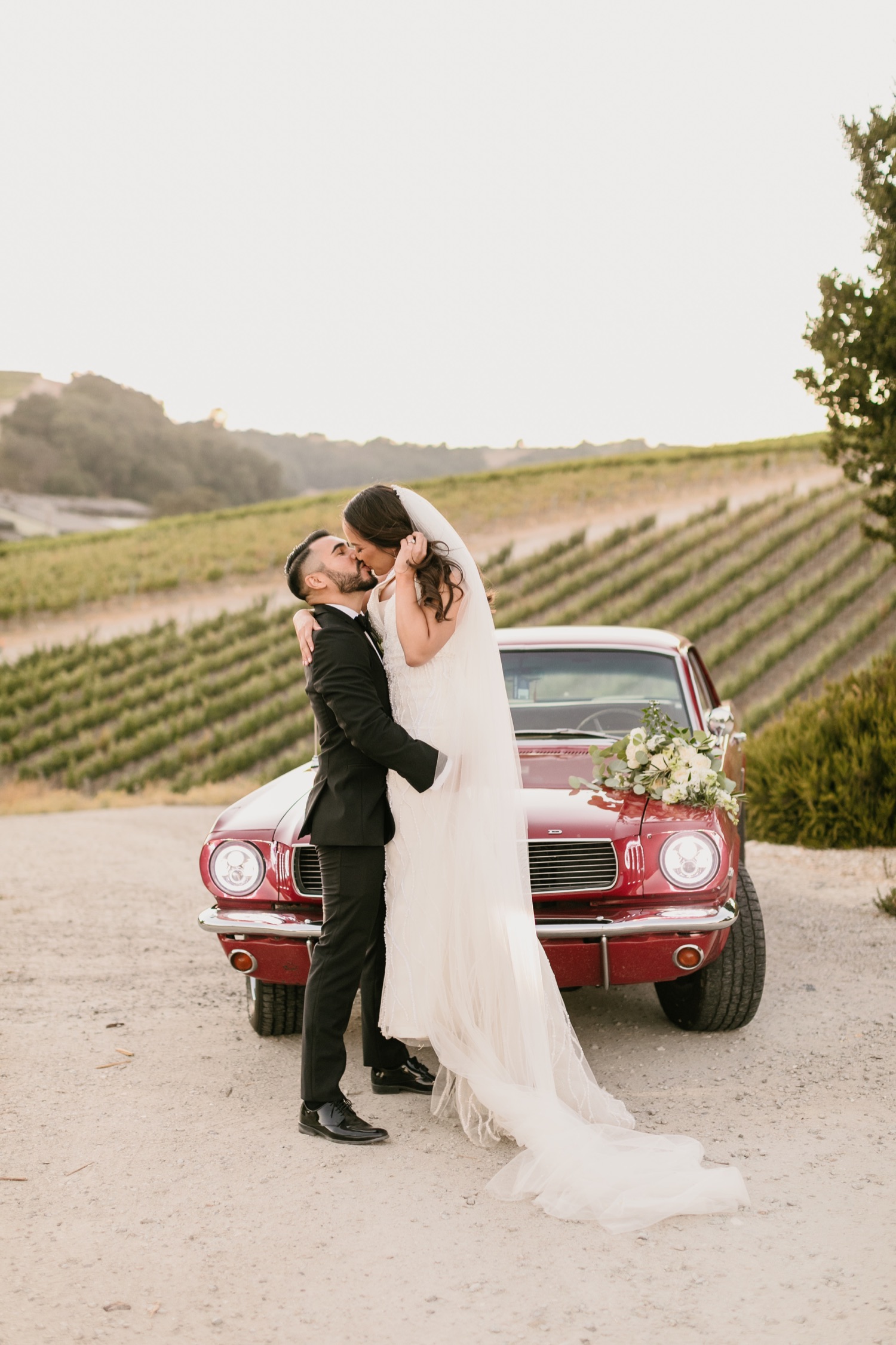bride and groom kissing in front of classic car at tooth and nail winery in paso robles california by tayler enerle