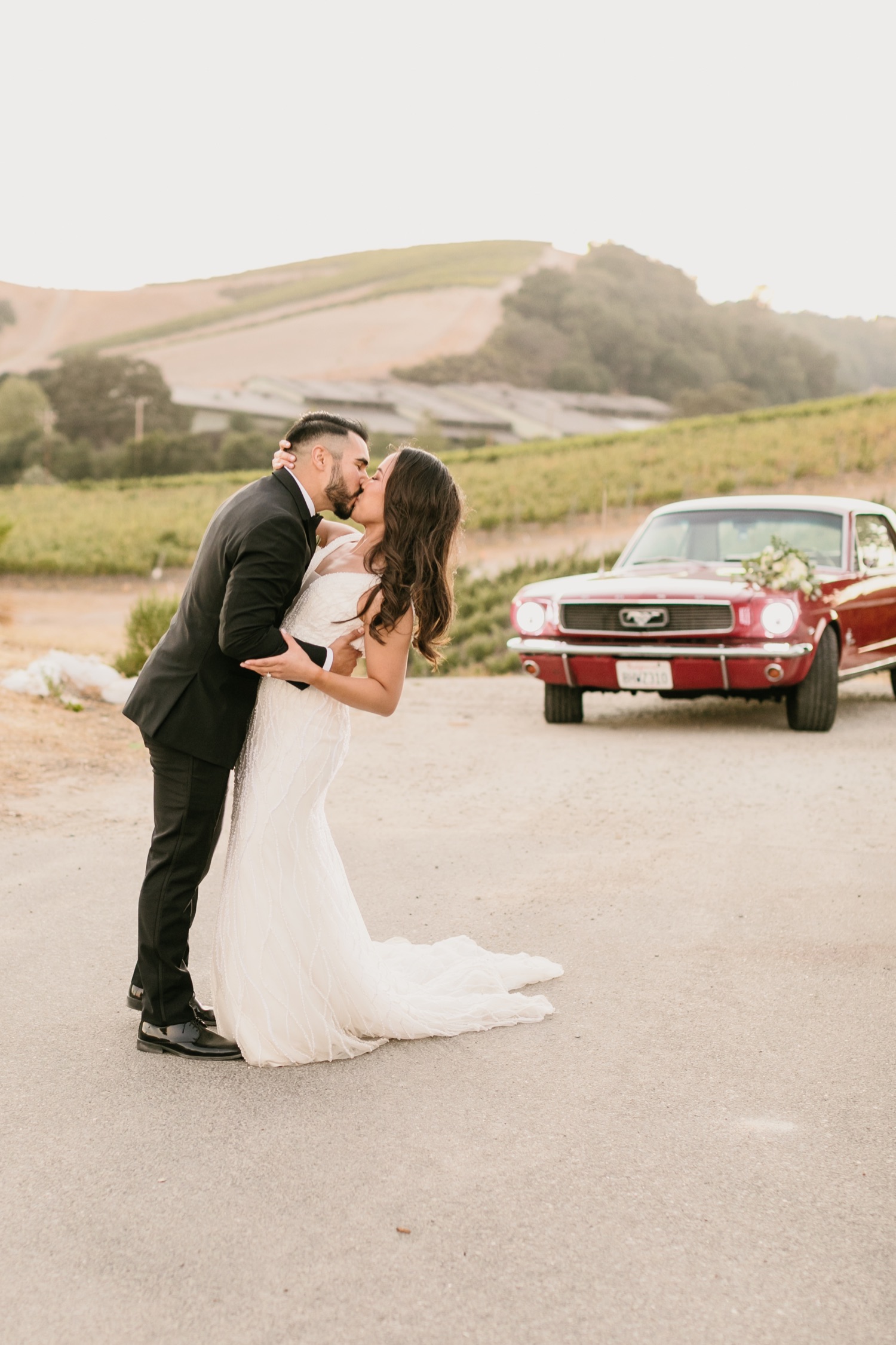 Bride and groom kiss in front of classic red car at tooth and nail winery