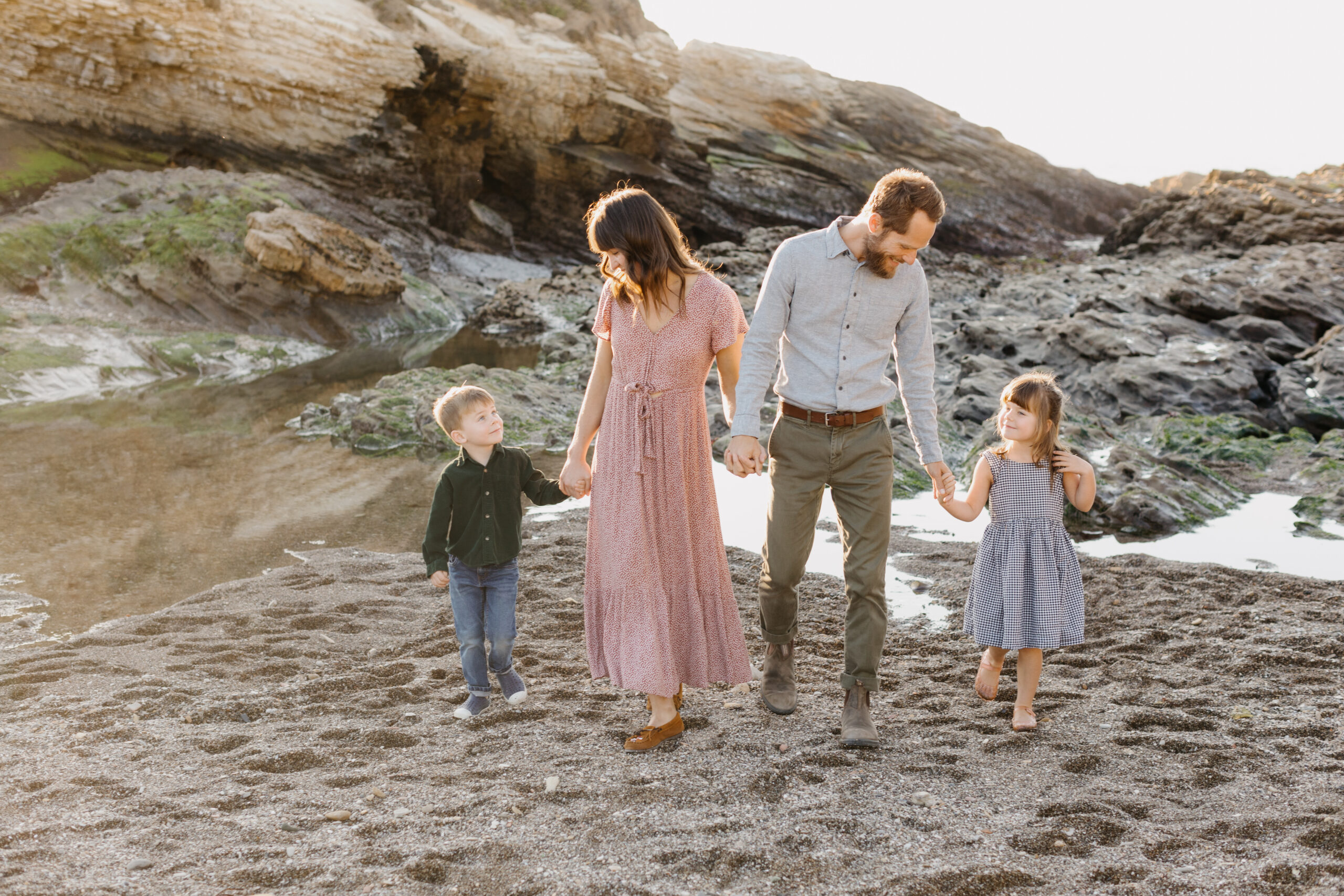 family walking together hand in hand looking at eachother happily while walking on the beach in Los Osos during their Montana De Oro family photographer session by Tayler Enerle
