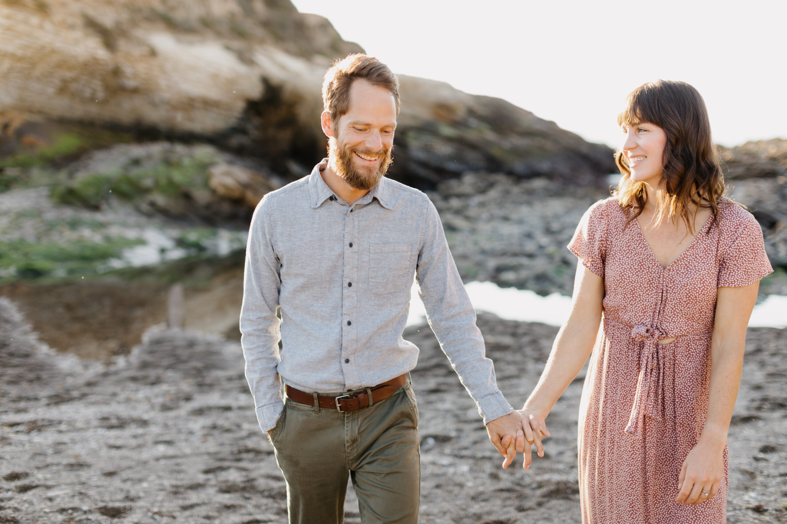 Couple walking hand in hand and smiling at each other at their family portrait at Montana De Oro in Los Osos California with photographer Tayler Enerle 