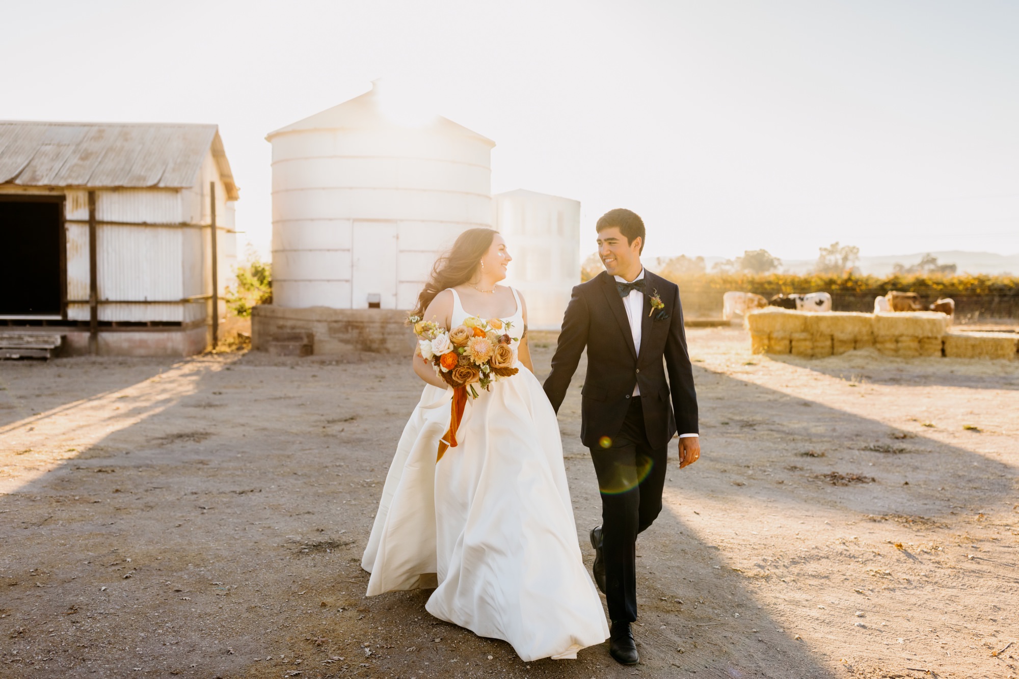 Couple running and looking at eachother smiling while walking in front of vintage Siloh at the sunset portraits with Paso Robles wedding photographer, Tayler Enerle, at 1800 El pomar wedding venue in templeton, california