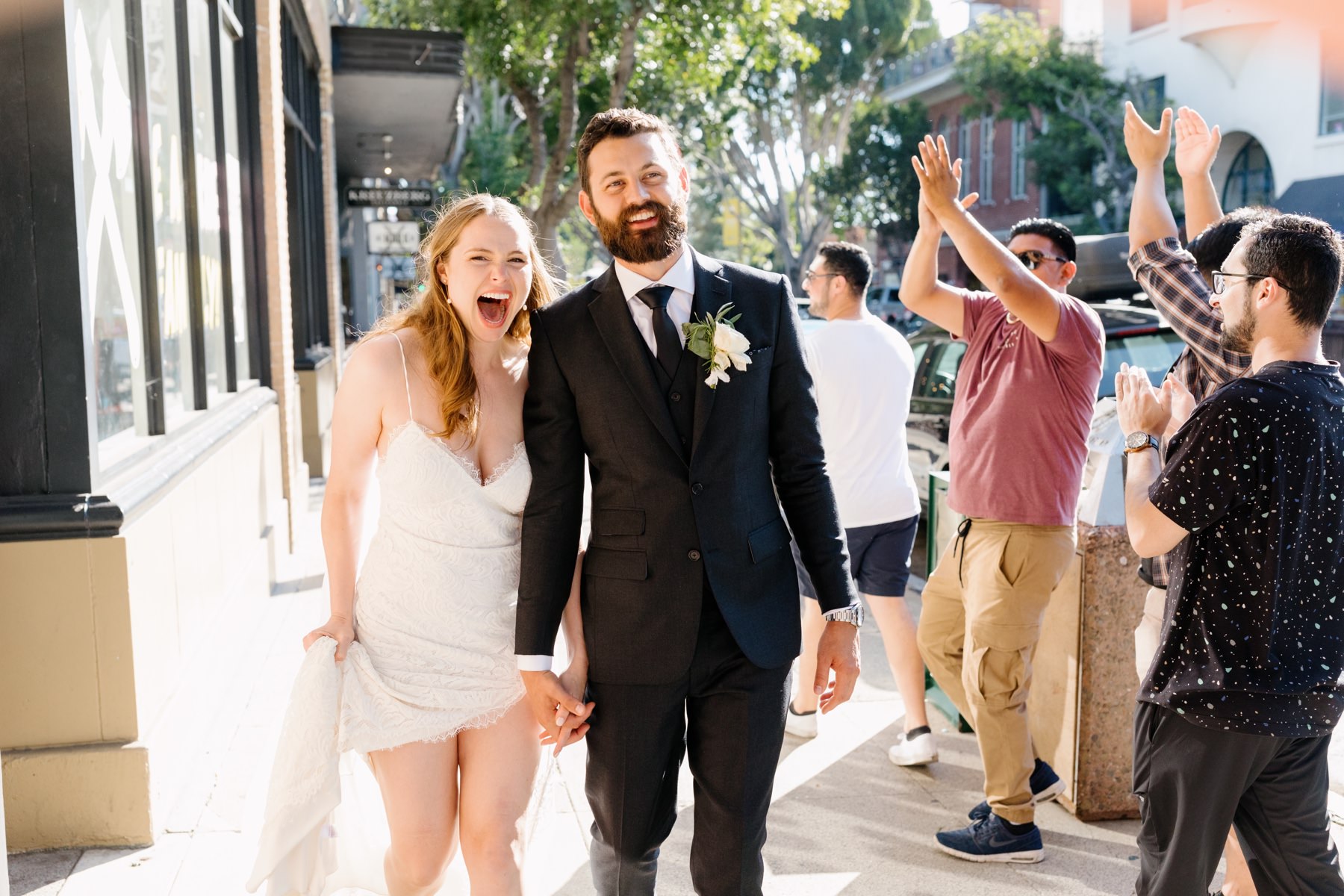 Newlywed bride and groom walking hand in hand downtown san luis obispo, california during their wedding reception at the Penny in Slo, with cheering strangers behind and next to them