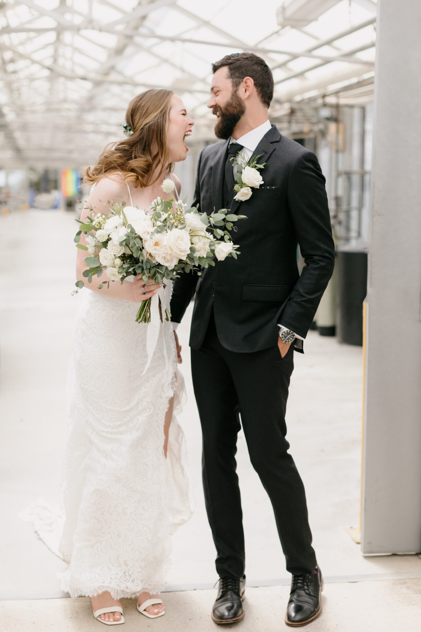 Couple smiling and laughing at each other during their portraits in the cal poly arboretum greenhouses during their wedding ceremony at Cal poly with the wedding reception at the Penny in downtown san luis obispo