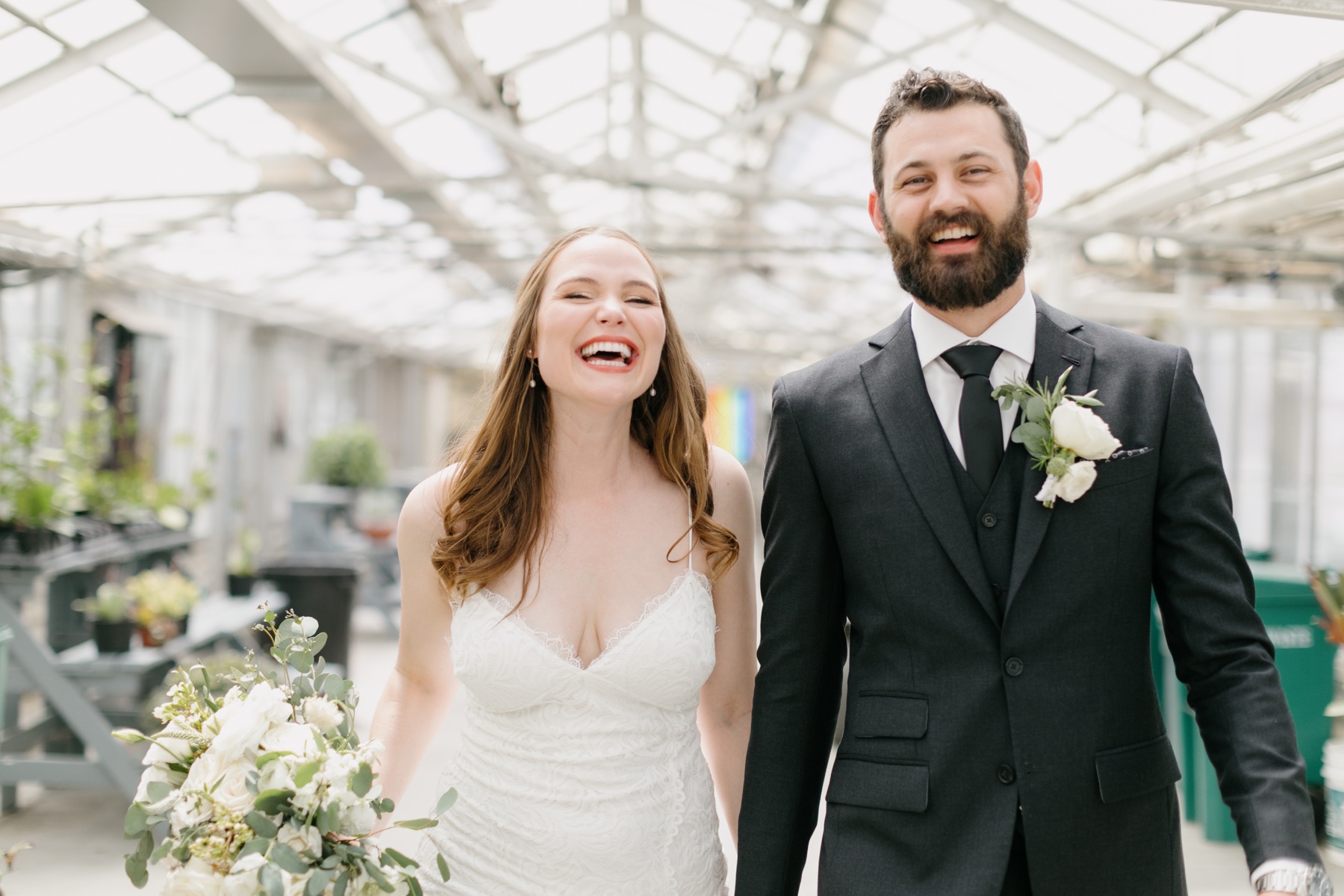 a newly married couple walking hand in hand and beaming with smiles through the cal poly arboretum green houses after their cal poly wedding ceremony in san luis obispo ca penny