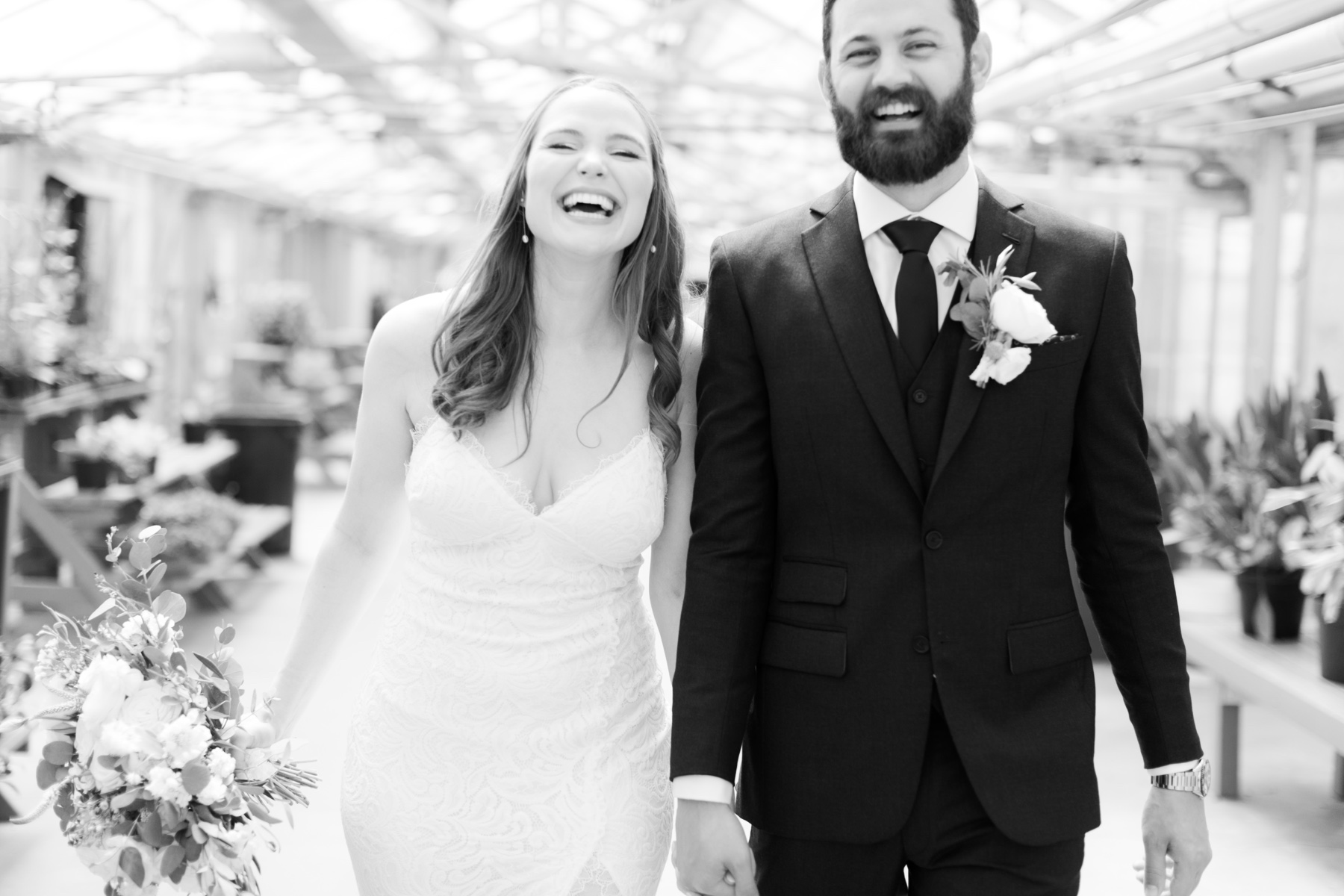 a bride and groom walking hand in hand and smiling while in movement in the cal poly greenhouses at the cal poly arboretum wedding ceremony