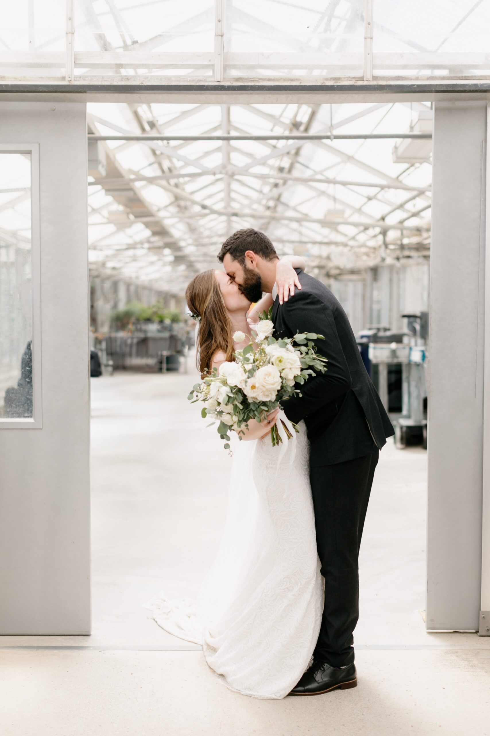 A couple embracing and kissing in the doorway of the greenhouses at cal poly arboretum before their ceremony on the lawn