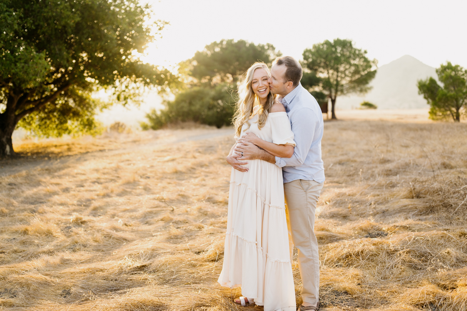 a man embracing his pregnant partner at their san luis obispo maternity session on terrace hill on a glowing sunny day