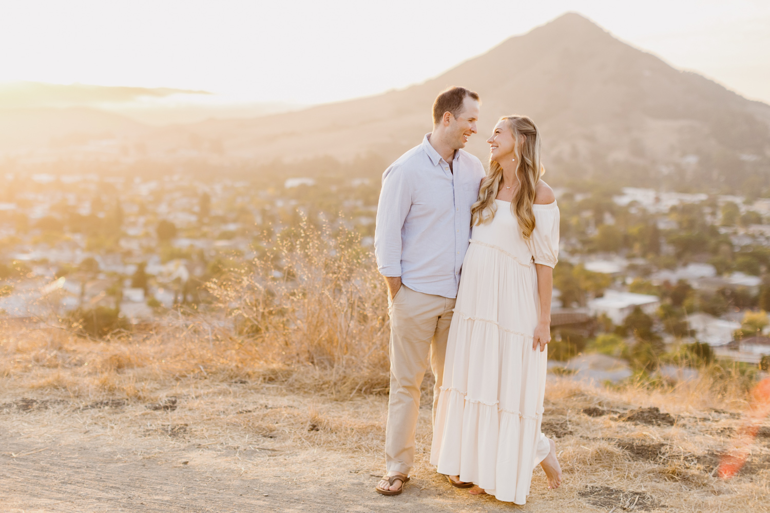 couple embracing and smiling at eachother overlooking slo at their san luis obispo terrace hill maternity session photographed by Tayler Enerle