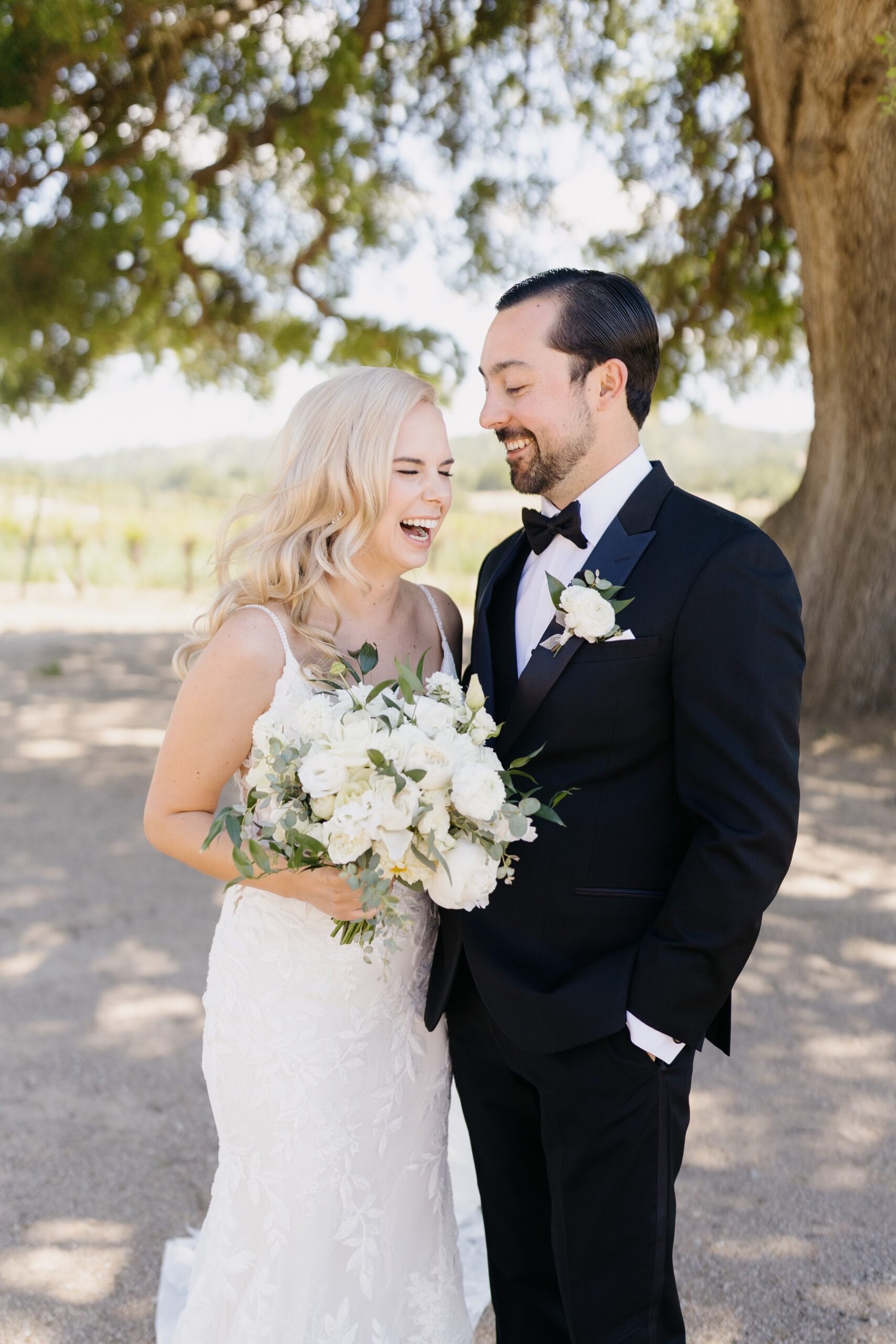 couple facing eachother and laughing on their wedding day in front of the oak tree at Cass Winery in Paso Robles california