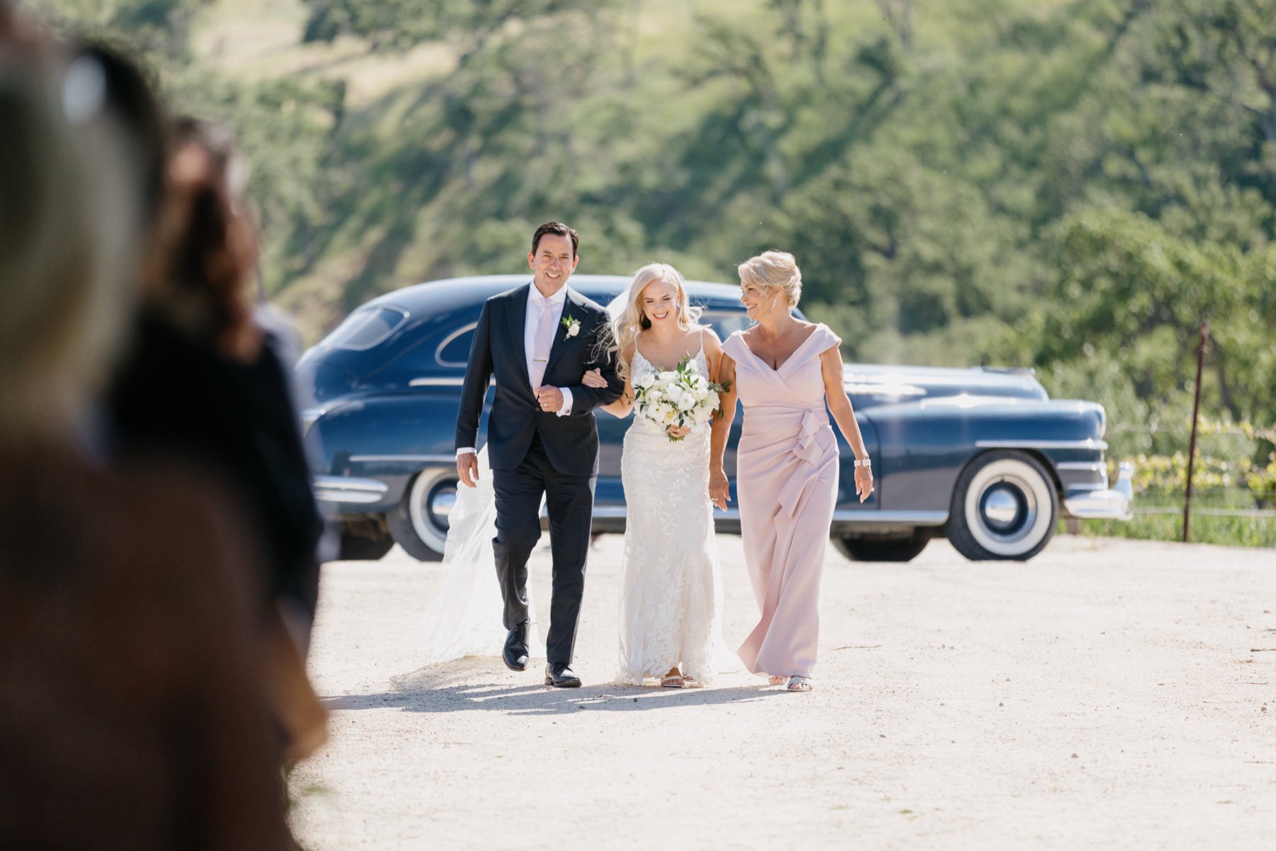 Bride walking with her mother and stepfather to her Cass Winery ceremony session where they were brought to the ceremony by a vintage car